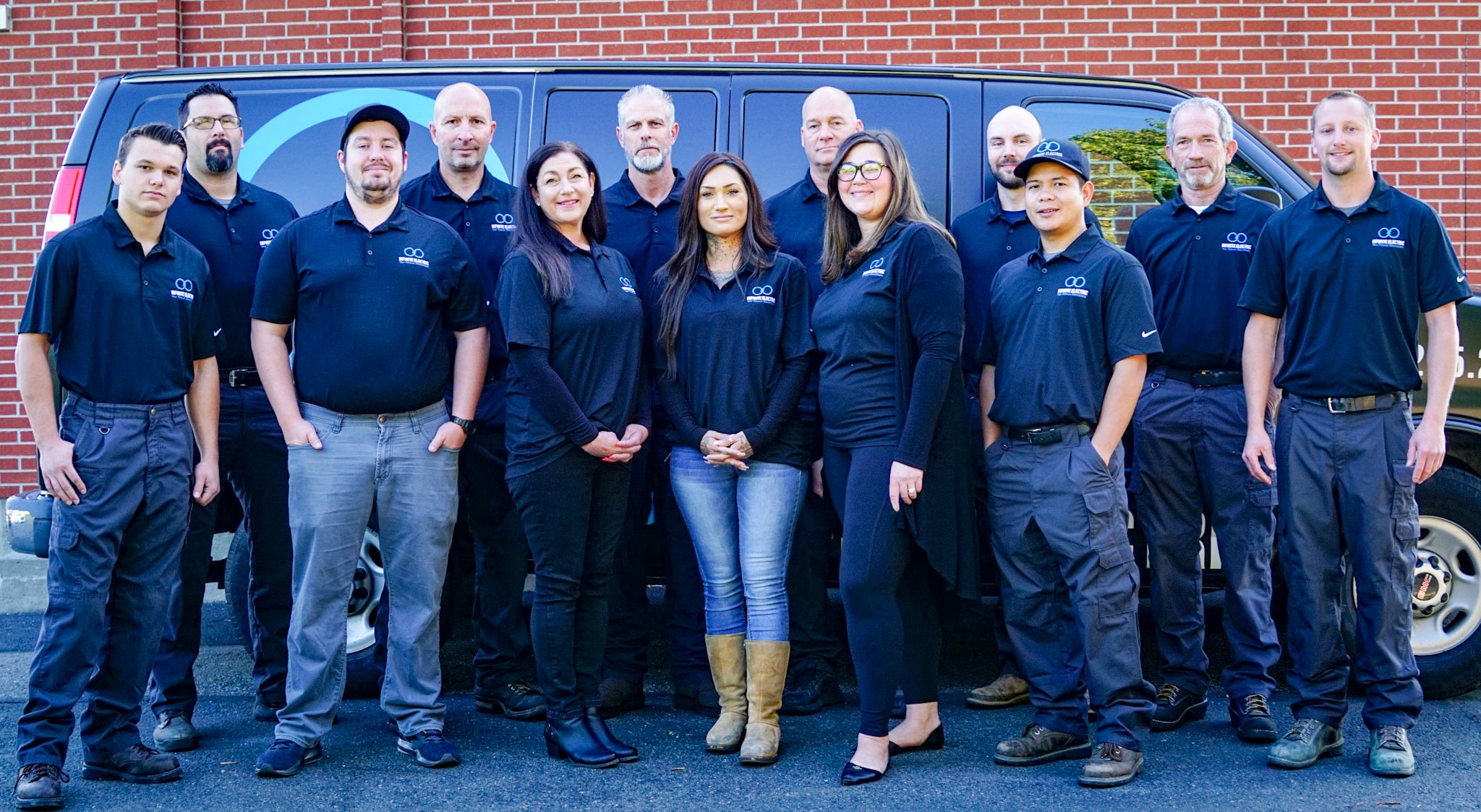 The full team of electricians at Infinite Electric standing in front of a service van.